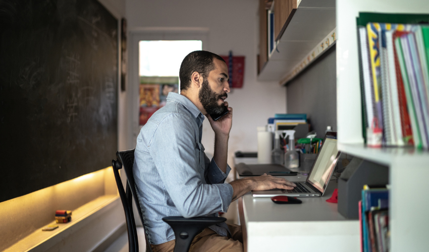 Man at desk on phone using laptop