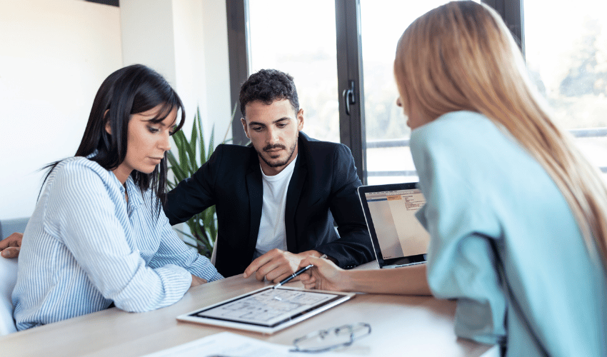 Three colleagues review plans on a tablet during a meeting in a bright office
